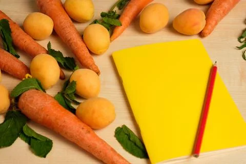 Yellow notepad with red pencil is surrounded by apricots and carrots on a wooden Stock Photos