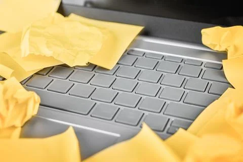 Yellow notes, some crushed, lie across a silver laptop keyboard. Stock Photos