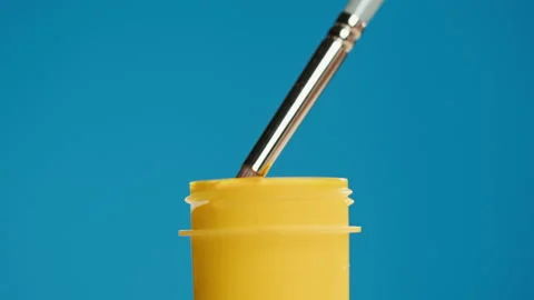 Yellow paint isolated on blue background. Bright gouache falling from paintbrush Stock Footage 178603185