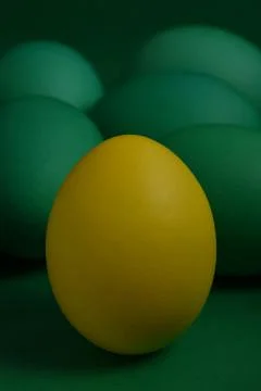 A yellow painted Easter egg stands in front of green eggs . Stock Photos