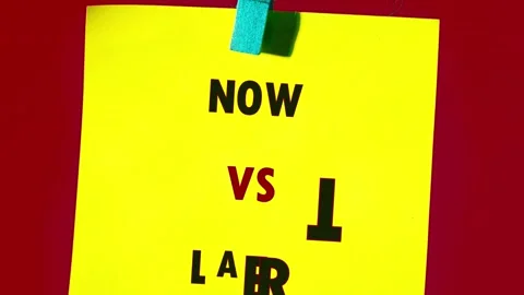 Yellow paper note displaying now versus later text held by a blue clothespin on Stock Footage 332691172