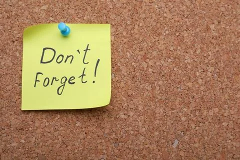 Yellow paper note with phrase Don't Forget pinned to cork board. Space for te Stock Photos