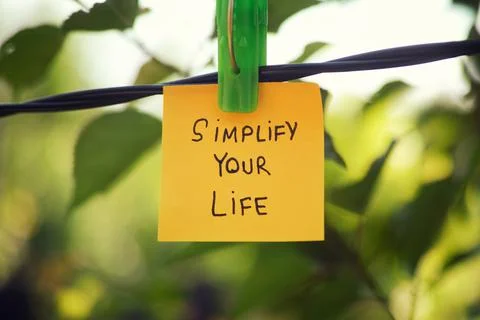 A yellow paper note with the phrase Simplify Your Life written on it hanging Stock Photos