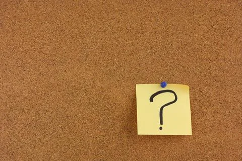 A yellow paper note with a question mark on it pinned to a cork board. Stock Photos