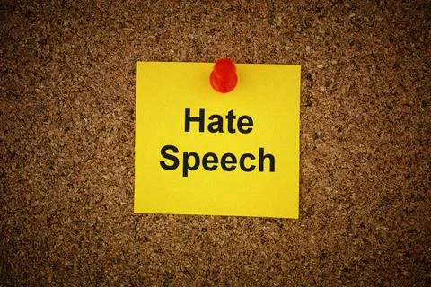 A yellow paper note with the words Hate Speech on it pinned to a cork board. Stock Photos