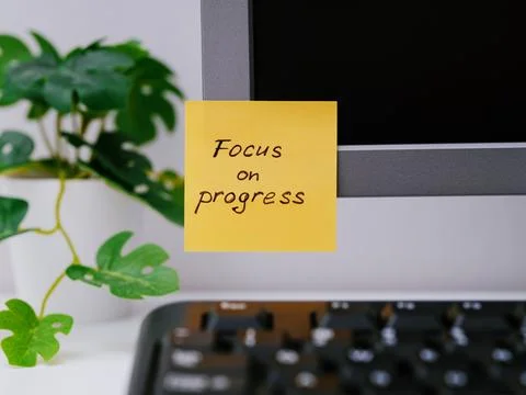 A yellow paper notes with the reminder Focus on Progress on it sticked on to  Stock Photos