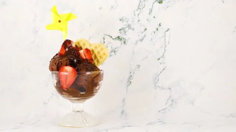Yellow paper windmill rotating on chocolate ice cream with strawberries 動画素材 130872906