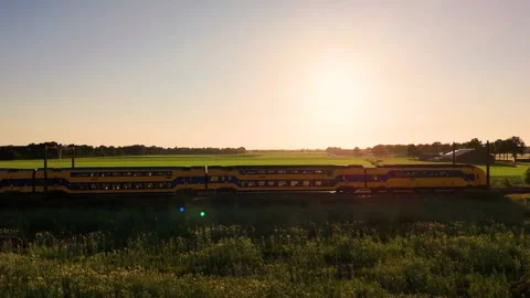 Yellow passenger train passing through green fields at sunset Stock Footage 314071097
