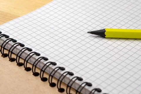 Yellow pencil on a notebook with sheets in a cage on a wooden table. Concept Stock Photos