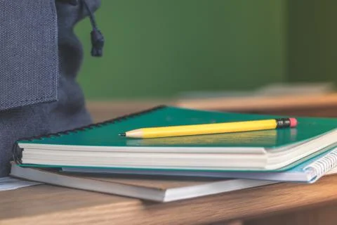 Yellow pencil on stack of study notebook on wooden table and blue backpack wi Stock Photos