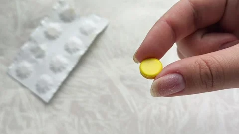 A yellow pill is in a womans hand, and there is a package of pills on the table Vídeo Stock 314880231