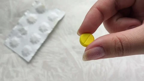 A yellow pill is in a womans hand, and there is a package of pills on the table Stock Footage 314880259