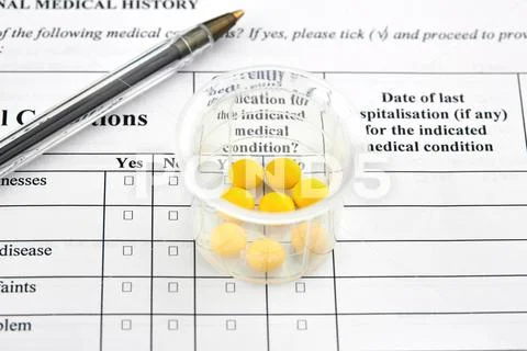 Yellow pills in graduated glass and pen on medical questionnaire form Stock Photos