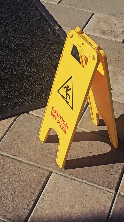 A yellow plastic "Caution Wet Floor" A-frame sign stands outdoor on stone pavers Video stock 335608567