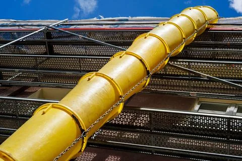 Yellow plastic debris chute on construction scaffolding against blue sky. L.. Stock Photos