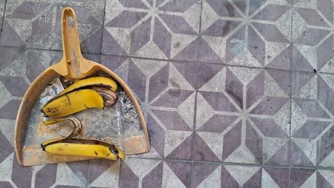 Yellow plastic dustpan containing discarded banana peels on patterned tiles Stock Photos