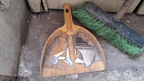 Yellow plastic dustpan containing sharp broken mirror shards and broom Stock Photos