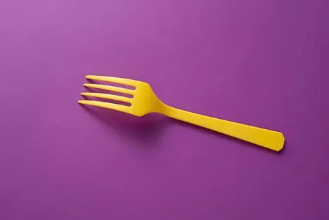Yellow plastic fork on purple background Stock Photos