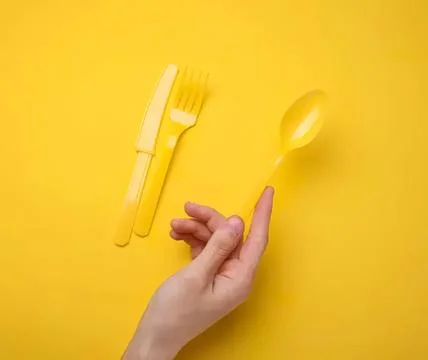 Yellow plastic fork spoon and hand on yellow background Stock Photos