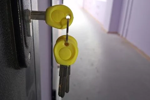 Yellow plastic-headed keys in lock on dark doorway in hallway setting Stock Photos