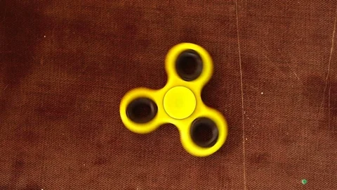 Yellow plastic spinner spinning on a wooden background. Slow motion. Stock Footage