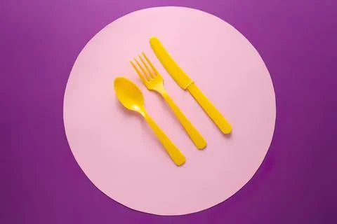 Yellow plastic spoon fork and knife on pink and purple background 스톡 사진