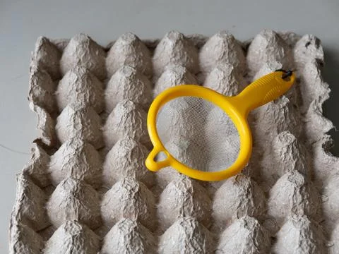 Yellow plastic strainer on empty egg carton tray Stock Photos