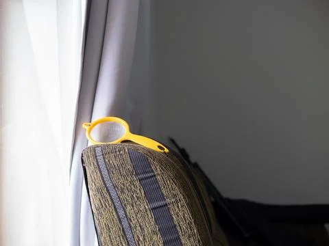 Yellow plastic strainer on striped sofa arm near window Stock Photos