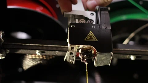 Yellow plastic thread that is printed by 3D printer head hand pushes green cable Stock Footage 124384773