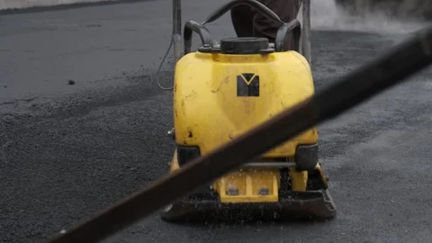 Yellow plate compactor working on fresh asphalt with roller background 库存影片 339802433
