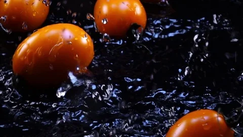 Yellow plum tomatoes with stems, falling on black surface with shallow water Stock Footage 78355219