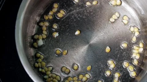 Yellow popcorn seeds exploding on a hot metal frying pan with oil. Stock Photos
