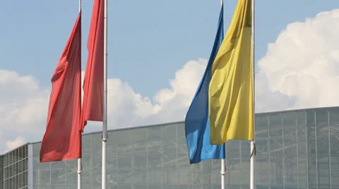 Yellow, red and blue flags waving against a blue sky and modern building Stockbeeldmateriaal 25418324