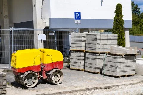 Yellow-red machine for compacting soil and road tiles at a construction site. Stock Photos