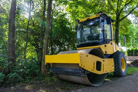 Yellow road roller on the background of forest and lawn. Stock Photos