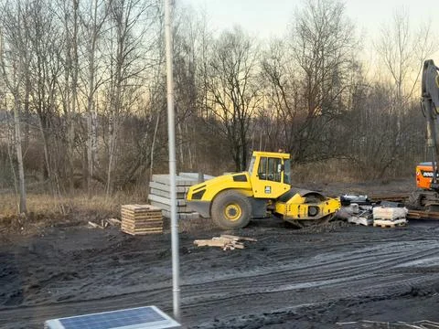 A yellow road roller parked at a construction site with stacks of concrete Stock Photos