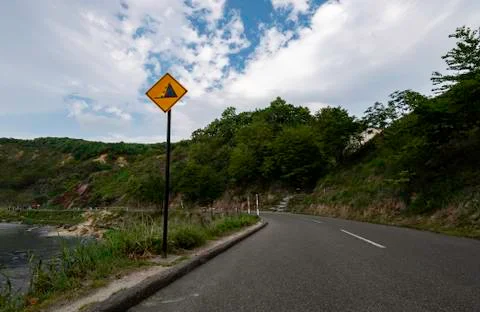 Yellow rock falling down warning sign in small road near mountain Stock Photos