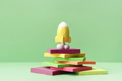 Yellow rocket stands on pile of note pads on green desk Stock Photos