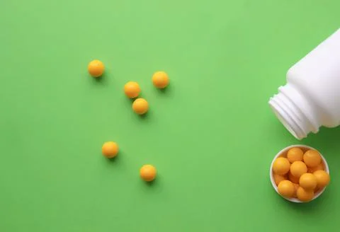 Yellow round tablets on a green background. Yellow vitamins from a white jar Stock Photos