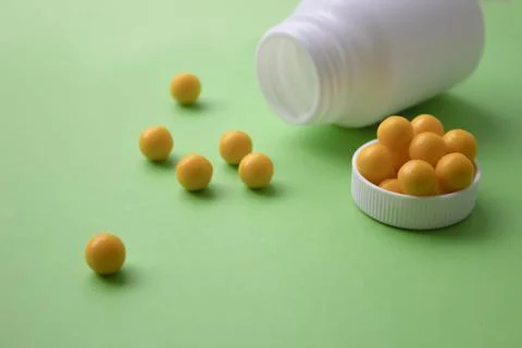 Yellow round tablets on a green background. Yellow vitamins from a white jar Stock Photos