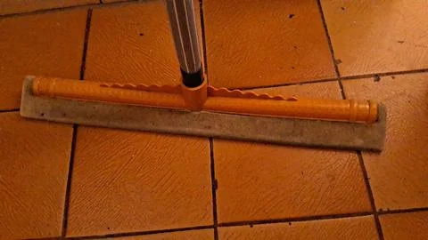 Yellow rubber floor squeegee resting on rustic orange tiled floor surface Stock Photos