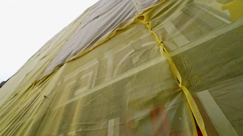 Yellow safety mesh covers scaffolding on a building facade during renovation Stock Footage 333430480