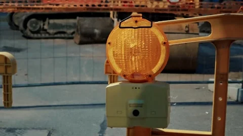 Yellow safety warning light blinking near heavy machinery at road repair site Stock Footage 334630808