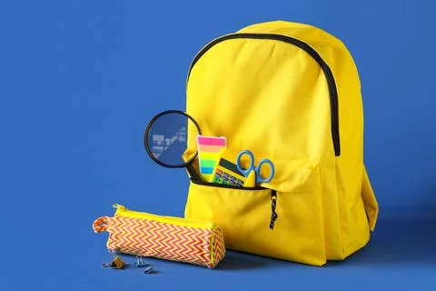 Yellow school backpack with different stationery and magnifying glass on blue Stock Photos