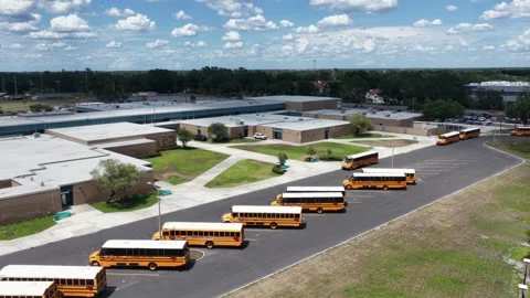 Yellow school buses queue in long rows across paved parking lot outside high Stock Footage 340044985