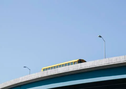 A yellow schoolbus driving over an elevated roadway against a blue sky. Stock Photos