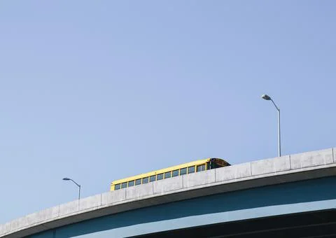 A yellow schoolbus driving over an elevated roadway against a blue sky. Foto stock