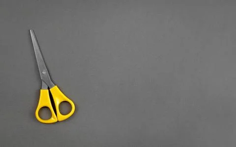 Yellow scissors lie on a gray background with the texture of thick paper Foto stock