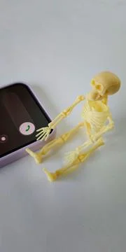 Yellow skeleton model sits next to a smartphone displaying a green call butto Stockfoto's
