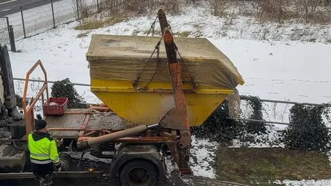 Yellow skip container being loaded onto a truck by a driver in a high Stock Photos